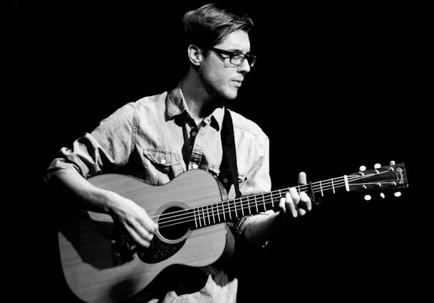 Man playing acoustic guitar in black and white.