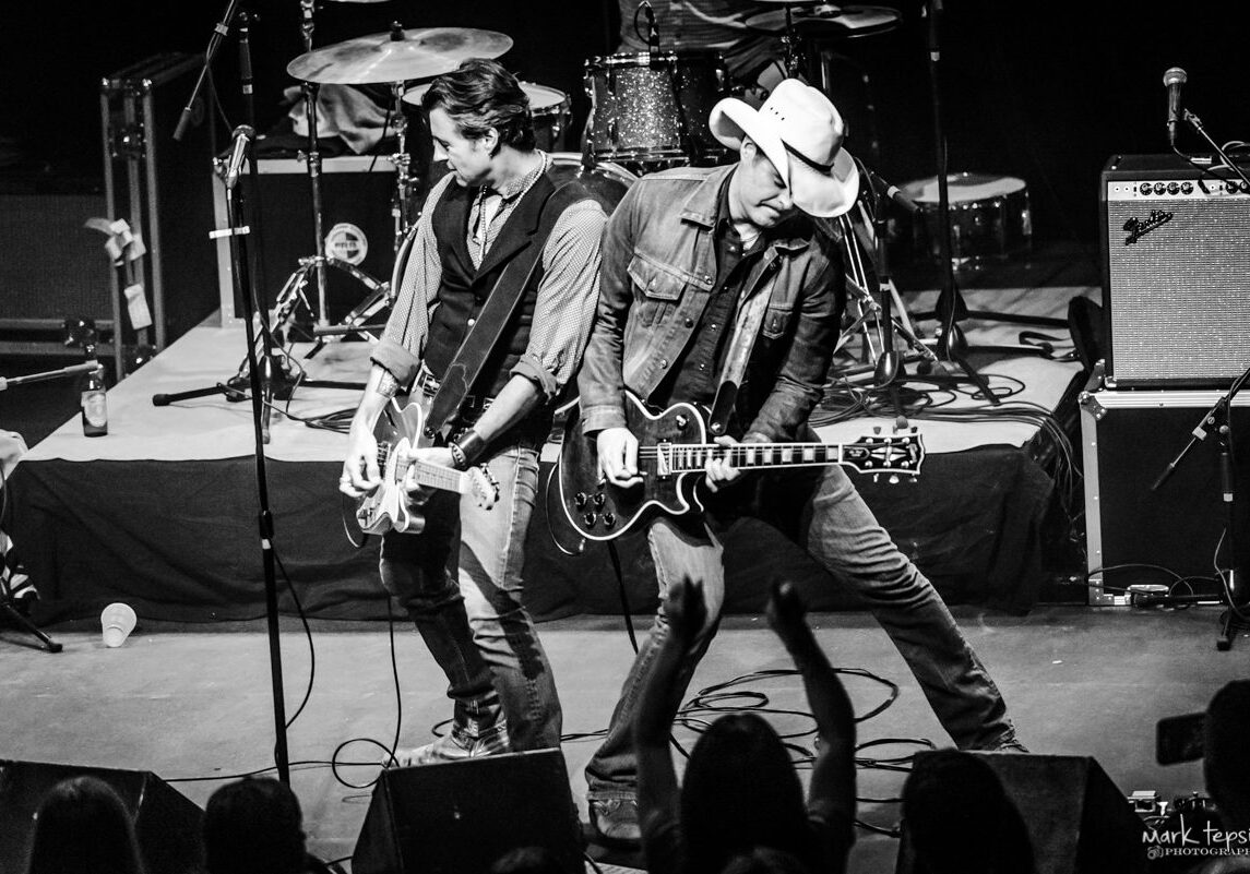 Two guitarists performing energetically on stage.