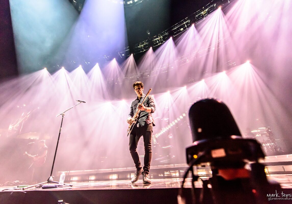 Guitarist performing on stage with dramatic lighting.