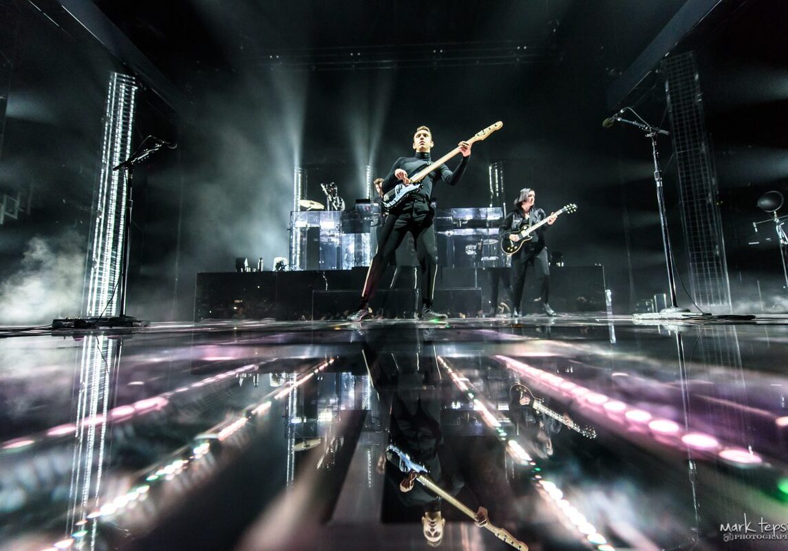 Band performing on stage with reflections.