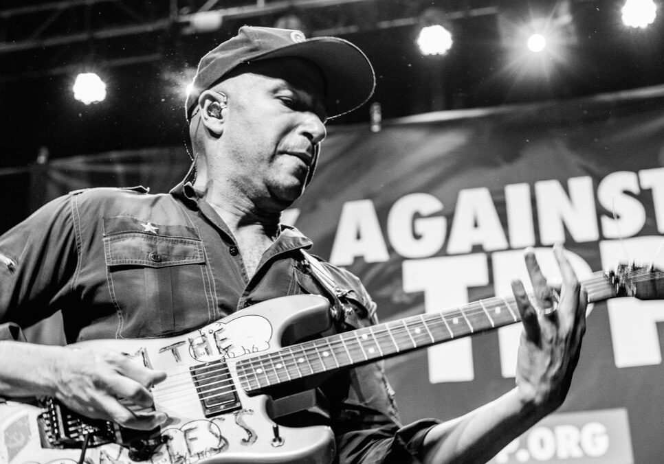 Guitarist performing on stage with banner backdrop.