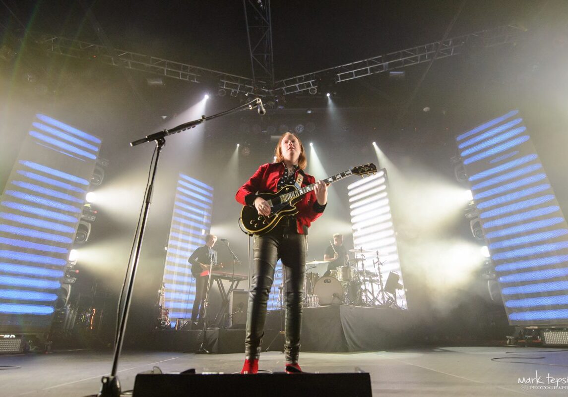 Guitarist performing on stage with bright lights.