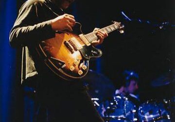 Guitarist performing on stage with drummer.