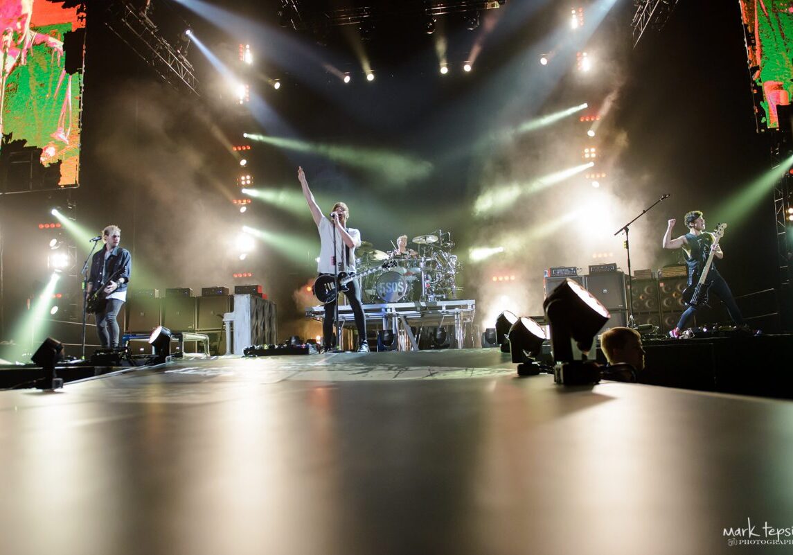 Rock band performing on brightly lit stage.