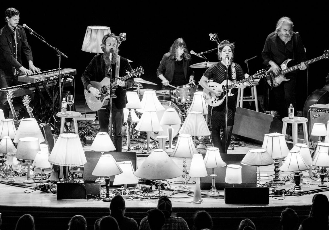 Band performing on stage with many lamps.