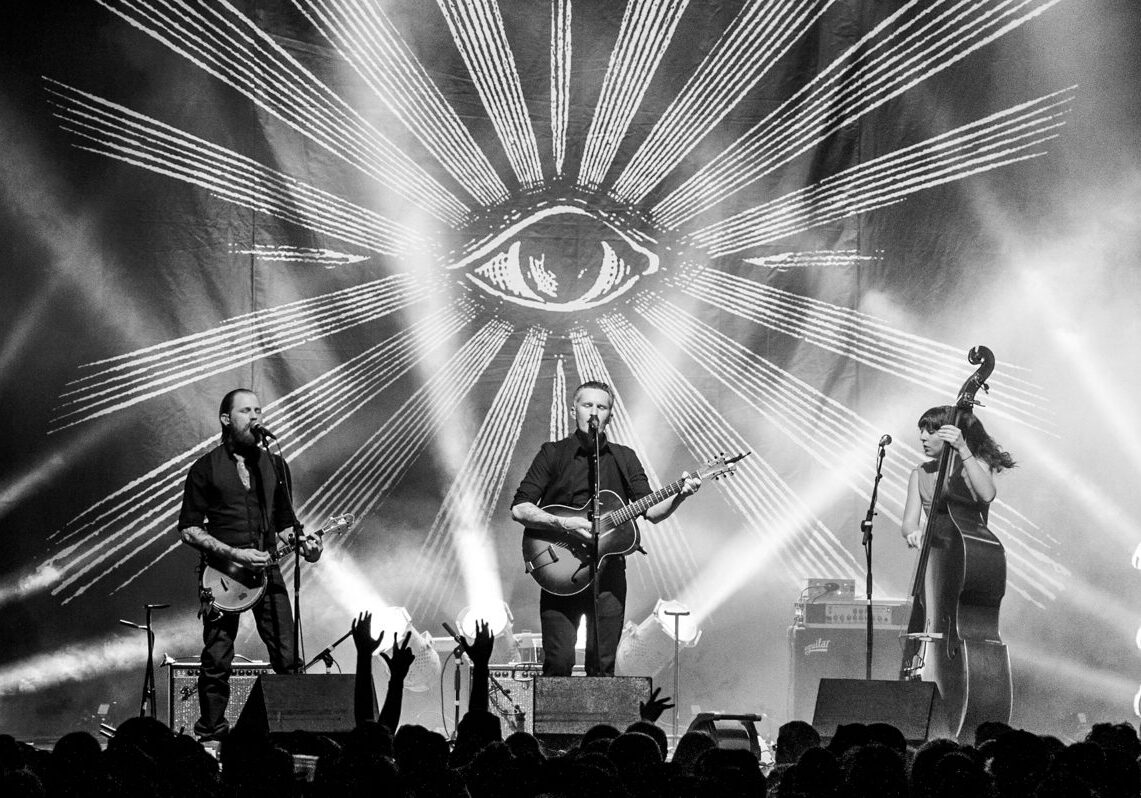 Band performing on stage with eye backdrop.