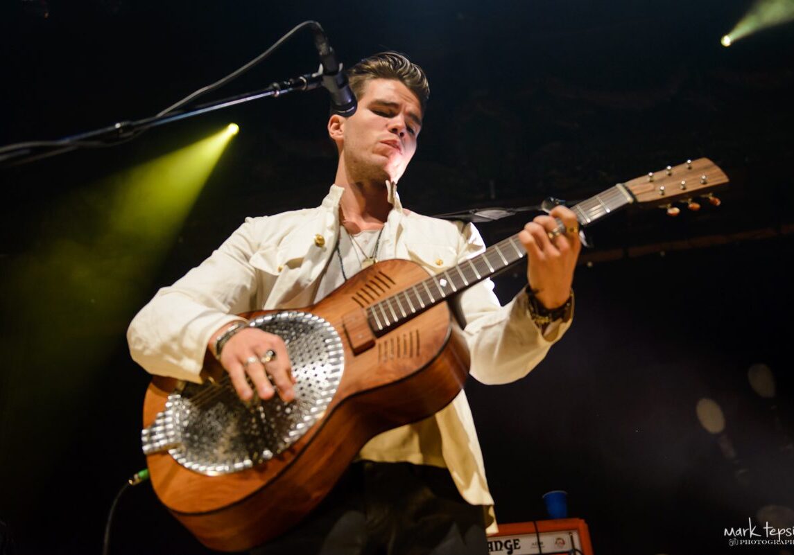 Musician playing guitar on stage under lights.