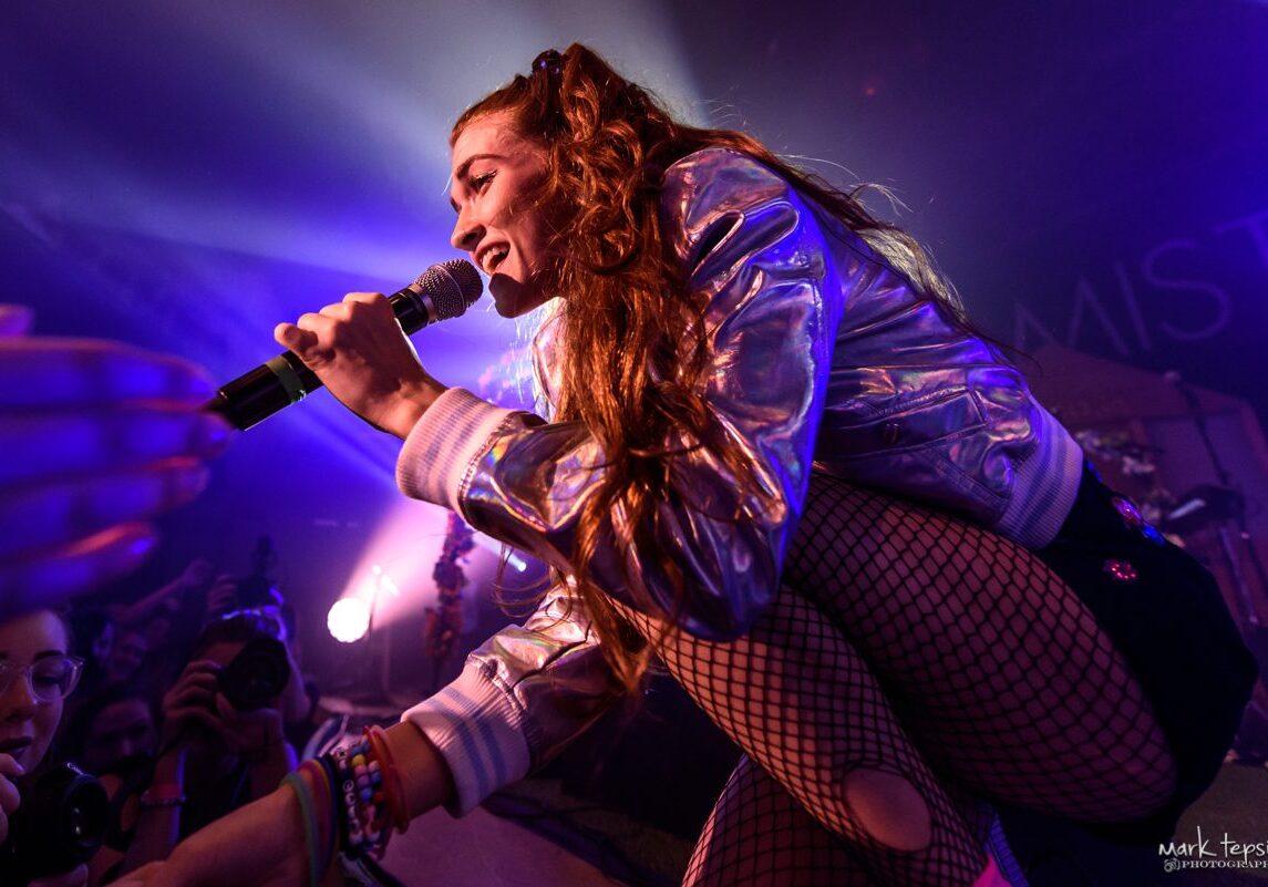 Singer performing energetically on stage with microphone.