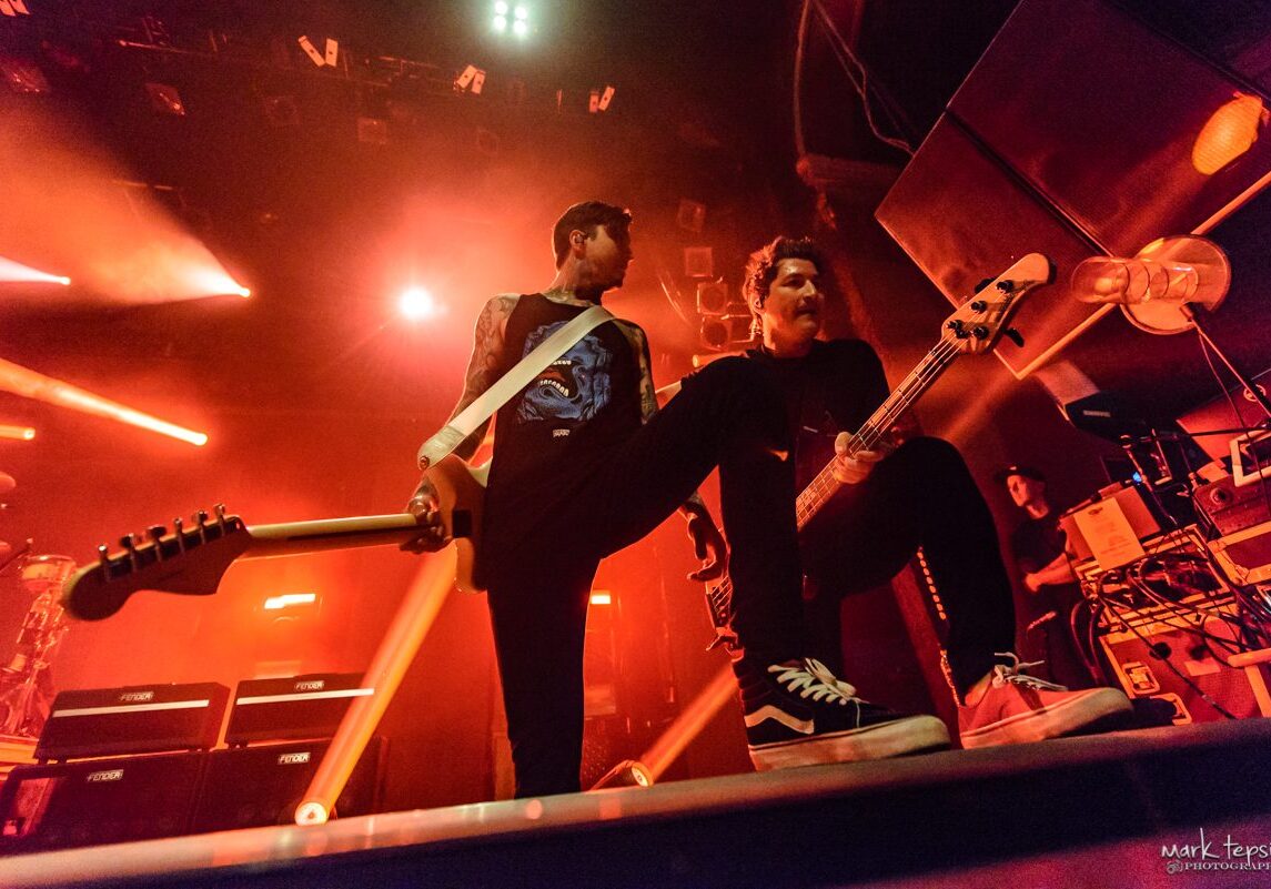 Musicians performing energetically on stage with guitars.
