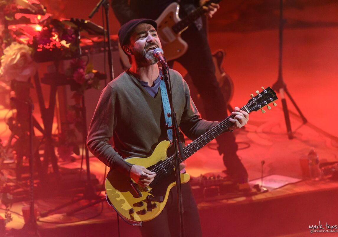 Musician performing on stage with guitar.