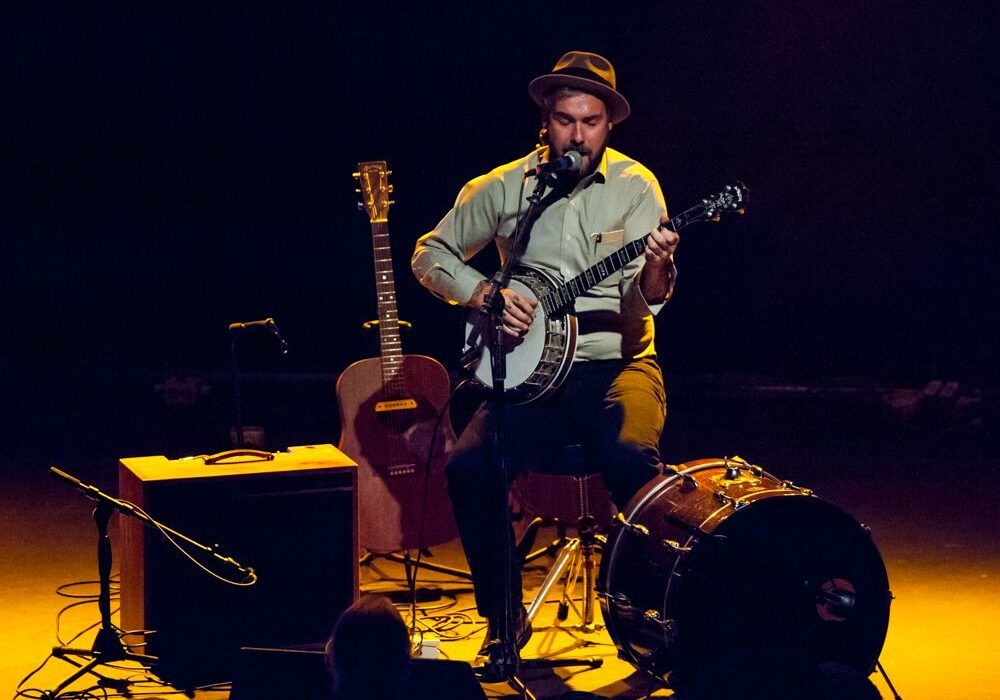 Musician performing on stage with guitar, banjo.