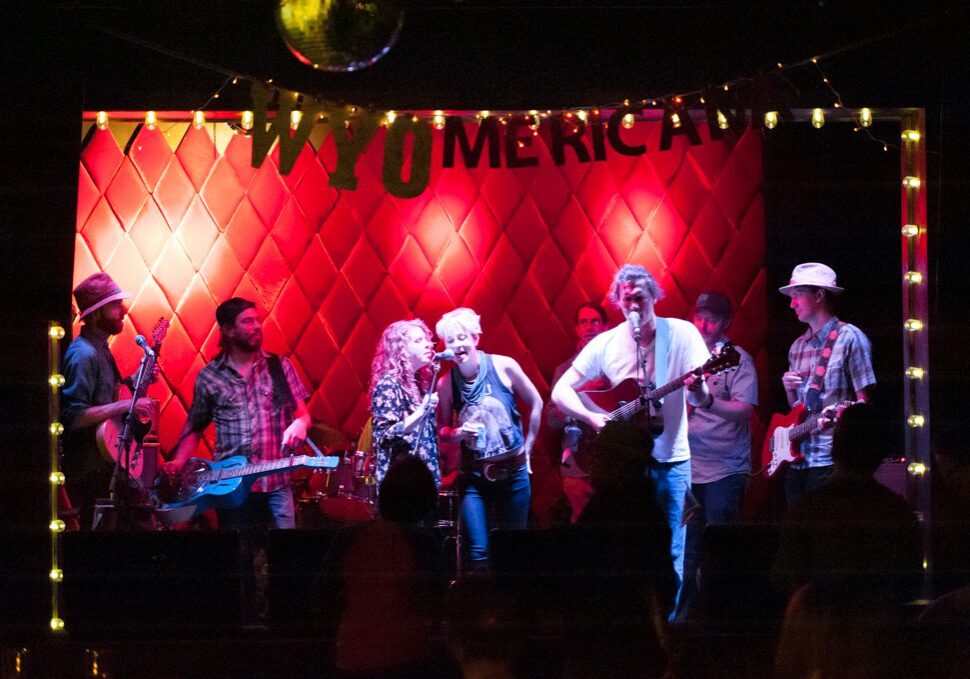 Band performing on stage with red backdrop.