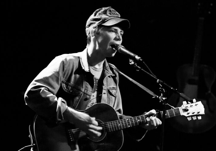 Musician singing and playing guitar on stage.