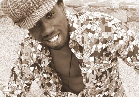 Man smiling in patterned shirt and cap.