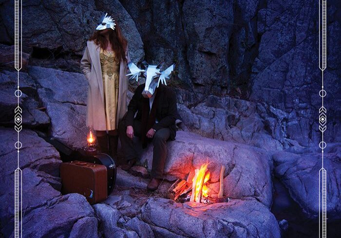 People with masks by a campfire.