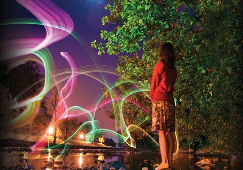 Girl standing by stream under colorful night sky.