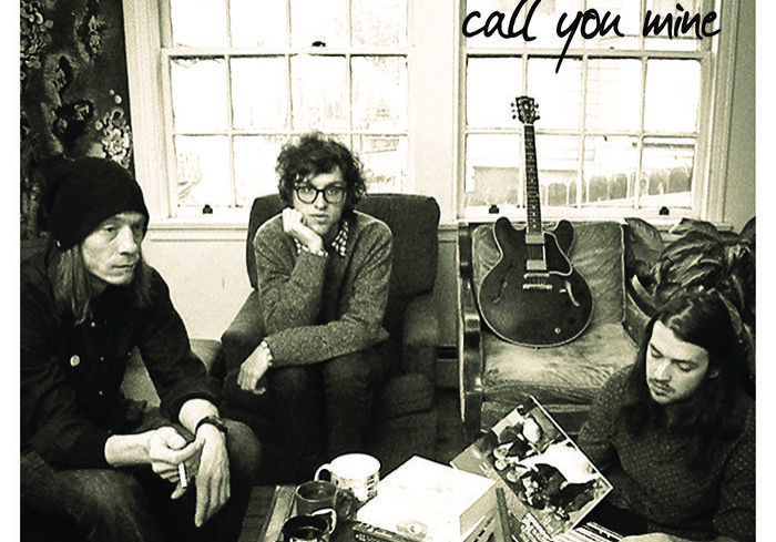 Band members sitting with records and guitar.