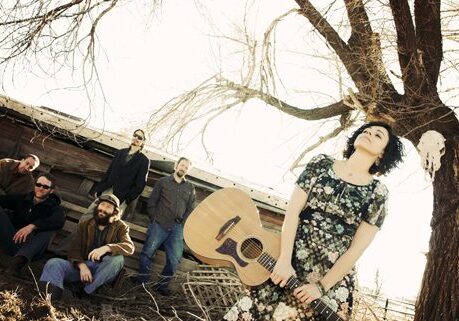 Band with guitar near tree and barn.