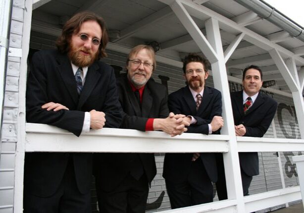 Four men in suits leaning on railing.