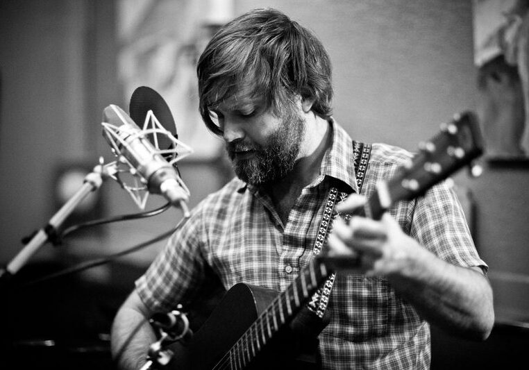 Musician playing guitar near a microphone.