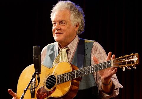 Elderly man playing guitar on stage.