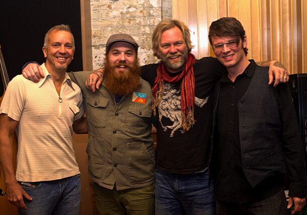 Four smiling men posing in casual attire.