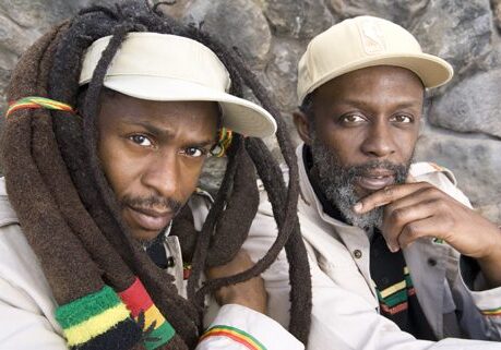 Two men wearing hats with dreadlocks.