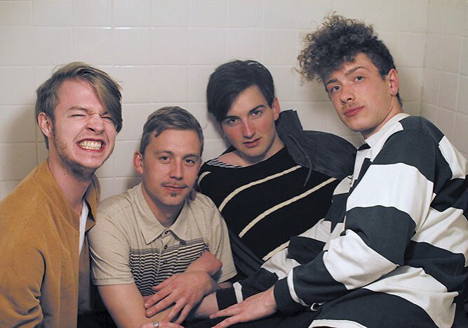 Four men sitting together in a bathroom.