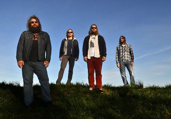 Four men standing on grassy hill.