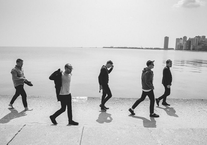 Five people walking along a lakeside promenade.