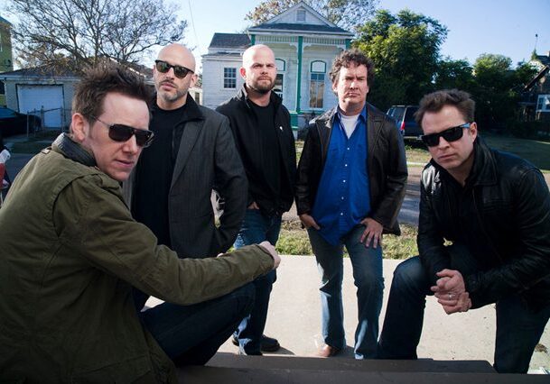 Five men posing outdoors, wearing casual attire.