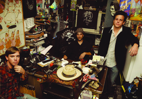Three men in a cluttered room.
