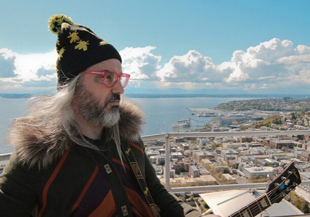 Man with guitar overlooking scenic cityscape.