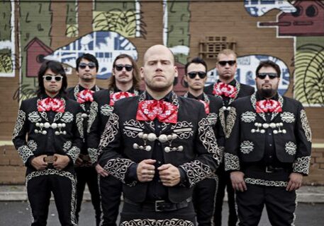 Group in mariachi outfits with mural background.