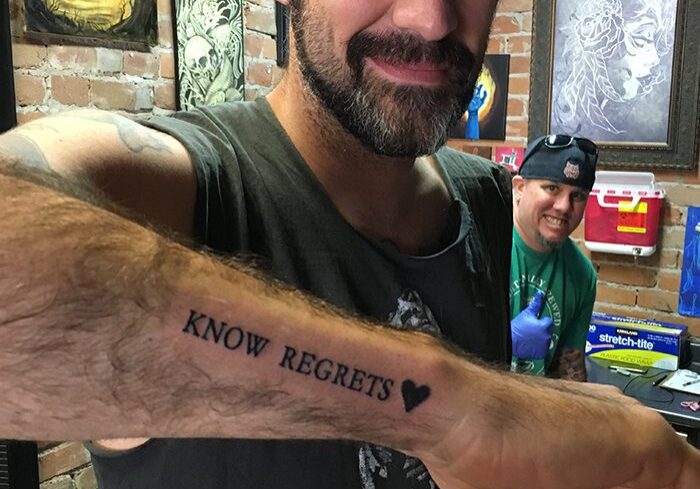 Man showing "Know Regrets" tattoo on arm.