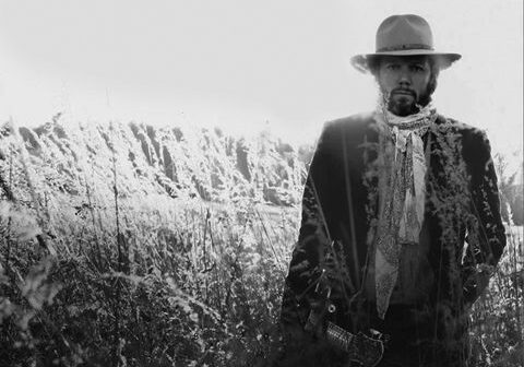 Man in hat standing in grassy field.