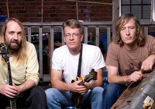 Three men with instruments sitting outside house.
