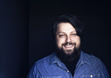 Smiling man with a beard and denim.