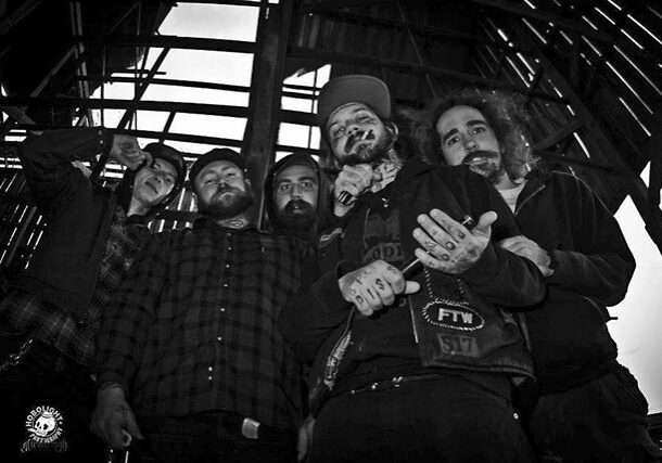Five men posing under wooden structure, monochrome.