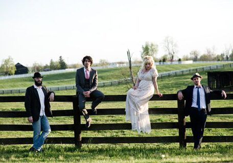 Four people sitting on a wooden fence.