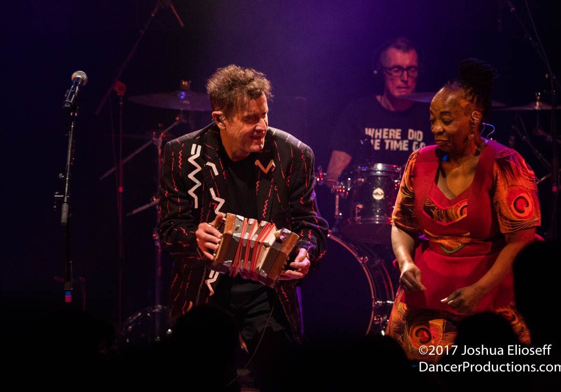 Musicians performing energetically on stage with instruments.
