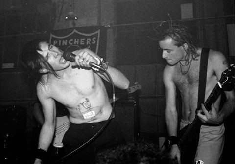 Two shirtless musicians performing energetically on stage.