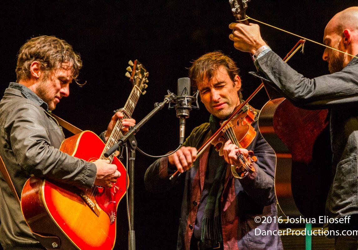 Three musicians performing with guitars and violin.