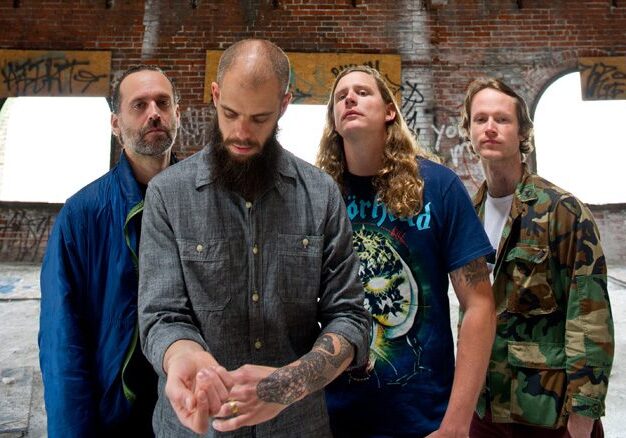 Four men standing in a graffiti-covered room.