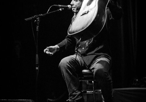 Musician performing with guitar on stage.