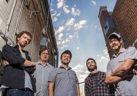 Five men standing in an alleyway, smiling.