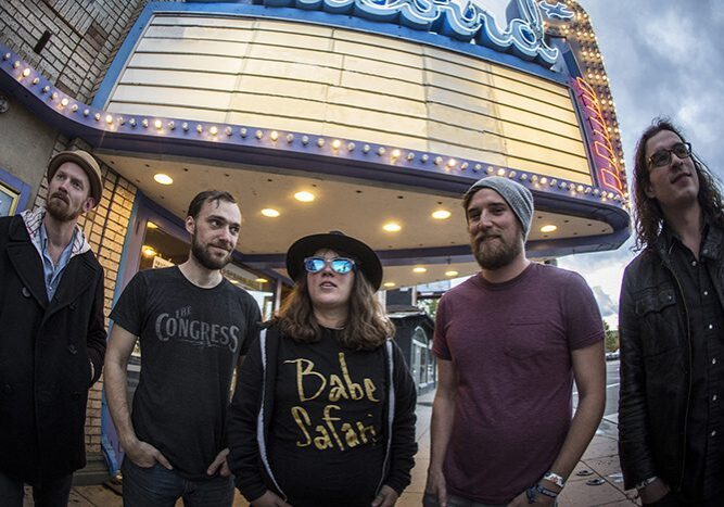 Five people standing under theater marquee.