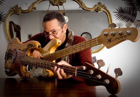 Man holding two electric bass guitars indoors.