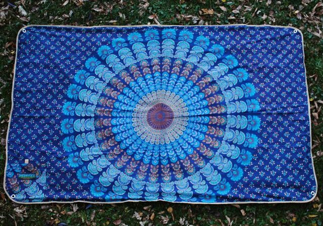 Blue mandala-patterned tapestry on grass background.