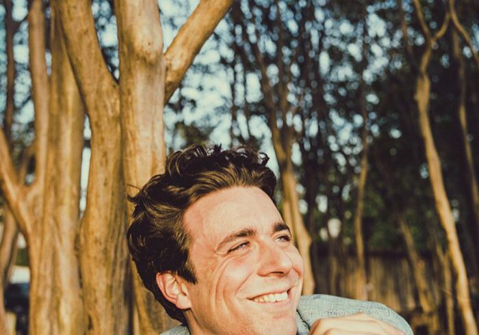 Smiling man outdoors near tall trees.